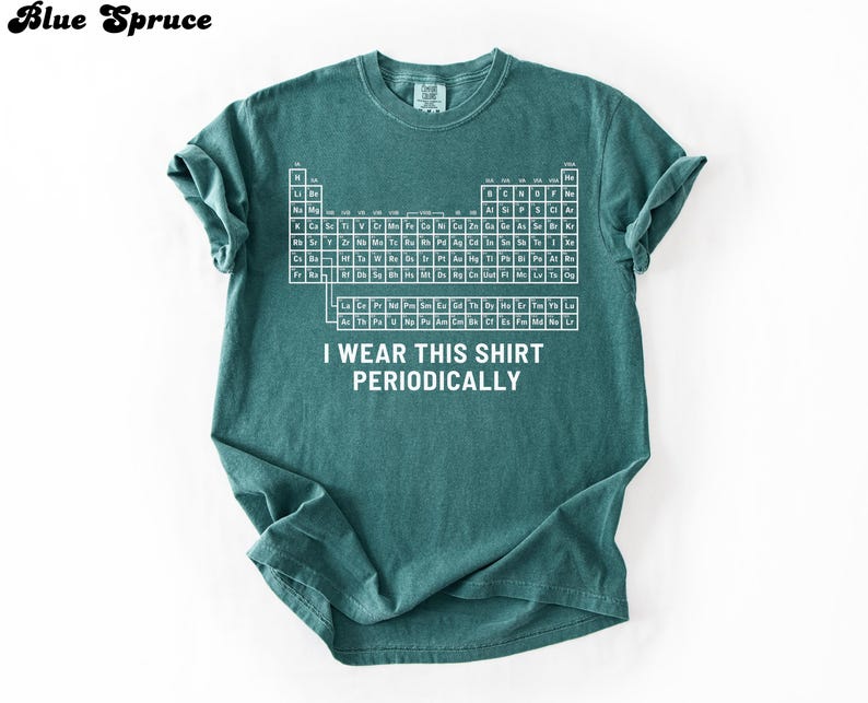 May include: Teal-colored t-shirt featuring a white periodic table design. The shirt includes the text "I WEAR THIS SHIRT PERIODICALLY" in white. The shirt is made of a soft material and has short sleeves.