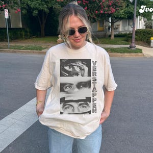 May include: Ivory-colored t-shirt featuring a black and white graphic of a person's eyes and face, with the name "VERSTAPPEN" printed vertically. The shirt is a relaxed fit and is being worn.