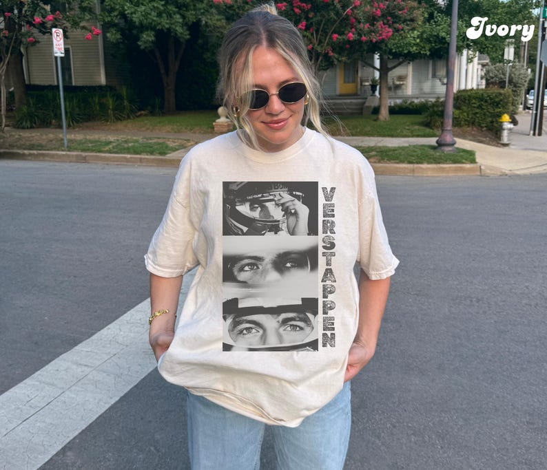 May include: Ivory-colored t-shirt featuring a black and white graphic of a person's eyes and face, with the name "VERSTAPPEN" printed vertically. The shirt is a relaxed fit and is being worn.