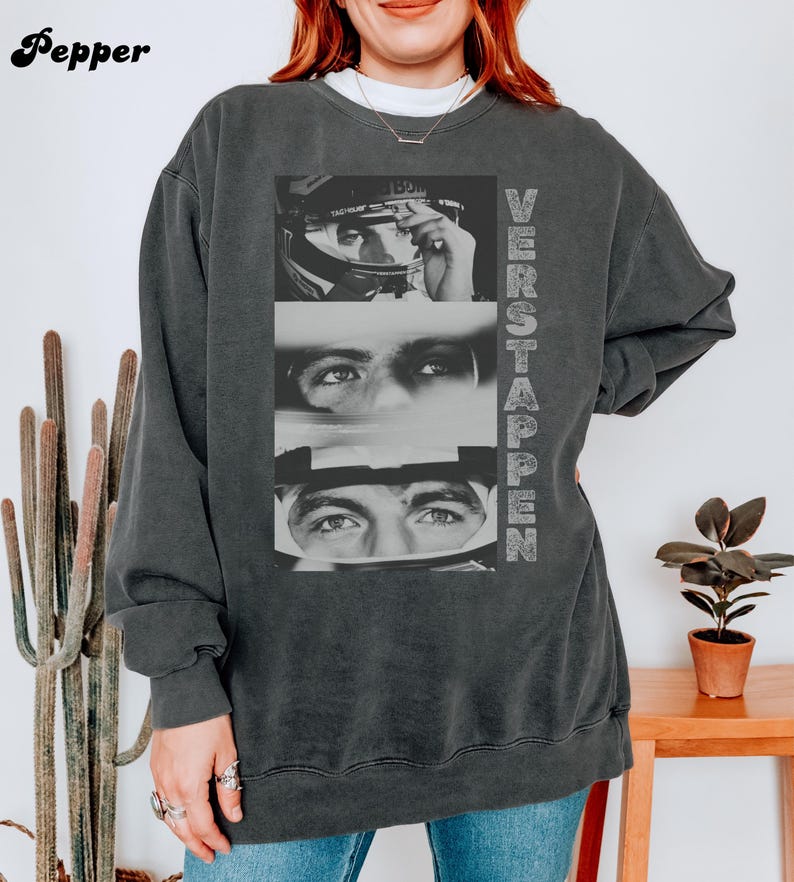 May include: Dark gray sweatshirt featuring a black and white image of a race car driver's face in three sections. The word "VERSTAPPEN" is printed vertically on the right side of the sweatshirt. The brand name "Pepper" is printed in the upper left corner.