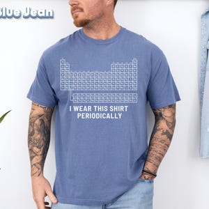 May include: A blue t-shirt with a white periodic table design and the text "I wear this shirt periodically." The shirt is made of a soft material and has short sleeves. The shirt is a solid blue color.