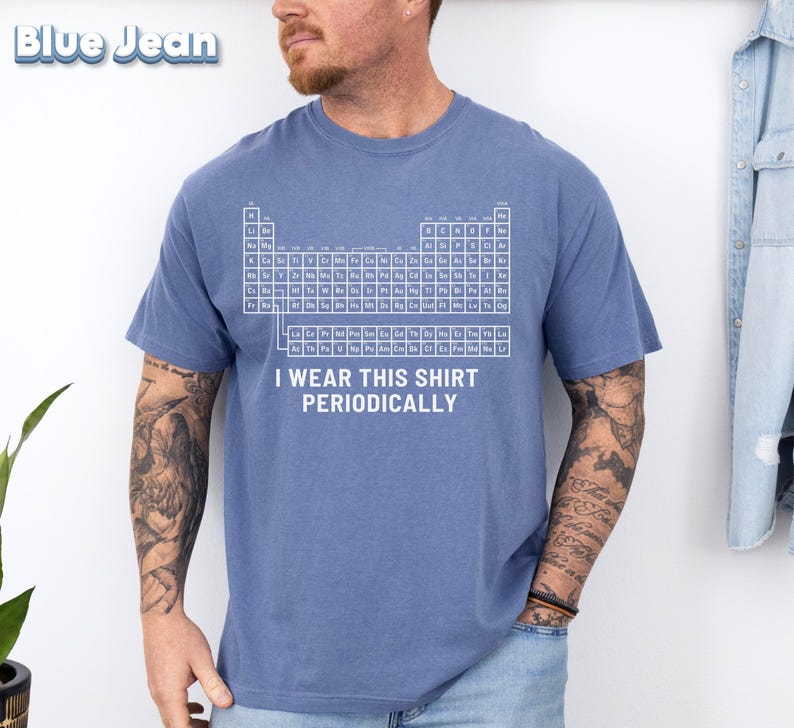 May include: A blue t-shirt with a white periodic table design and the text "I wear this shirt periodically." The shirt is made of a soft material and has short sleeves. The shirt is a solid blue color.