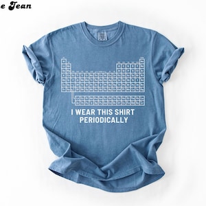May include: Blue jean colored t-shirt with a white periodic table graphic and the text "I wear this shirt periodically." The shirt is a short-sleeved crew neck.
