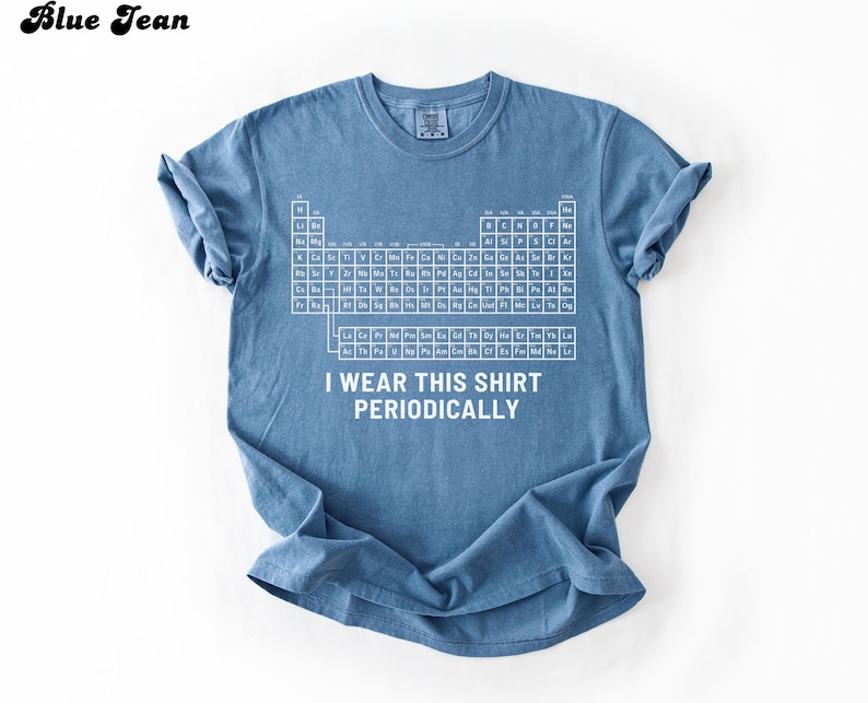May include: Blue jean colored t-shirt with a white periodic table graphic and the text "I wear this shirt periodically." The shirt is a short-sleeved crew neck.