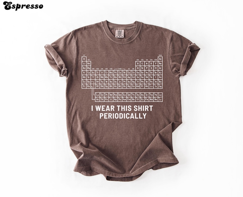 May include: Espresso-colored t-shirt with a white periodic table graphic and the text "I WEAR THIS SHIRT PERIODICALLY." The shirt has rolled sleeves and a relaxed fit. The shirt is made of a soft, comfortable material.