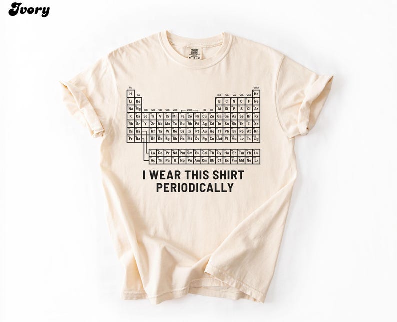 May include: Ivory-colored t-shirt featuring a black periodic table design. The shirt includes the text "I wear this shirt periodically" in a bold, sans-serif font. The shirt is made of a soft material and has short sleeves.