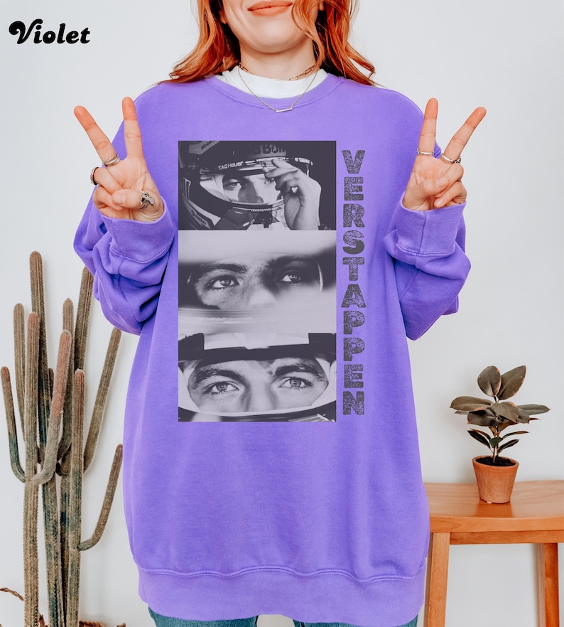 May include: A violet sweatshirt featuring a black and white image of a race car driver. The image is vertically stacked with the word "VERSTAPPEN" printed on the right side. The word "Violet" is printed in the upper left corner.