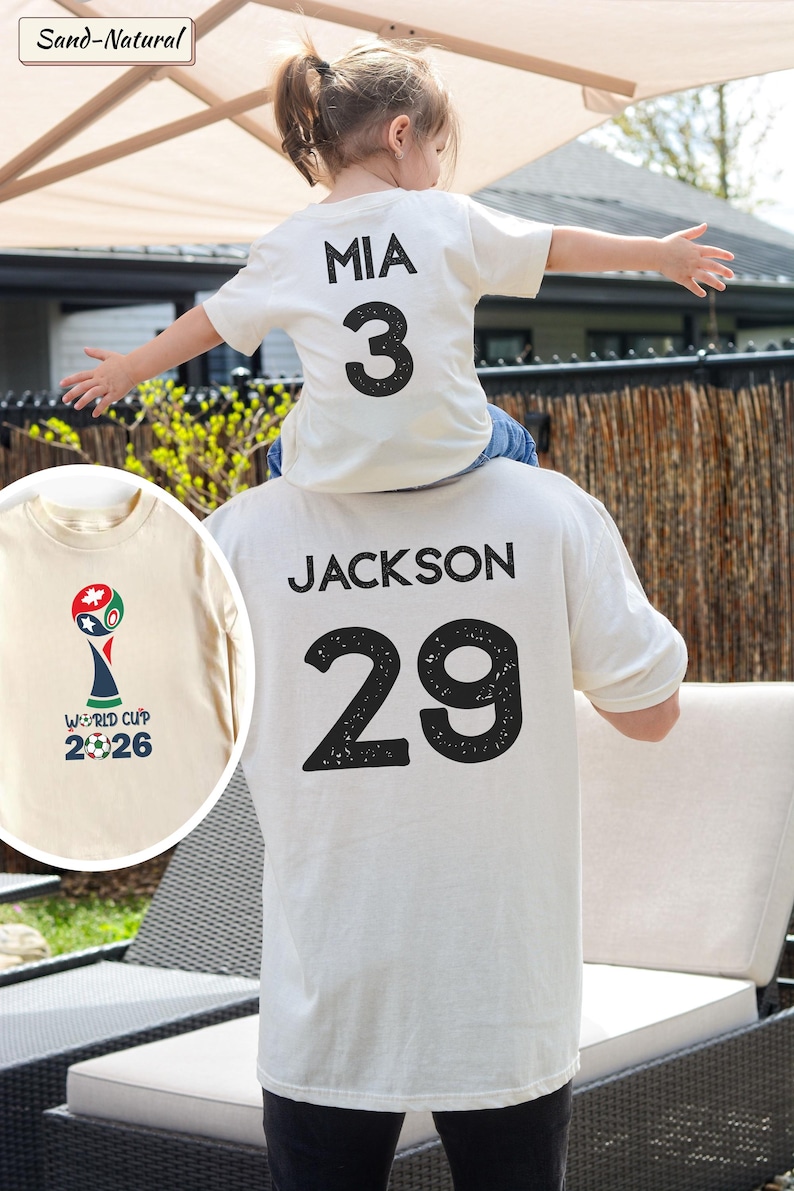 May include: A sand-natural colored t-shirt featuring the name JACKSON and the number 29 in black on the back. A smaller t-shirt in the same color displays the name MIA and number 3. A circular inset shows the World Cup 2026 logo in color.