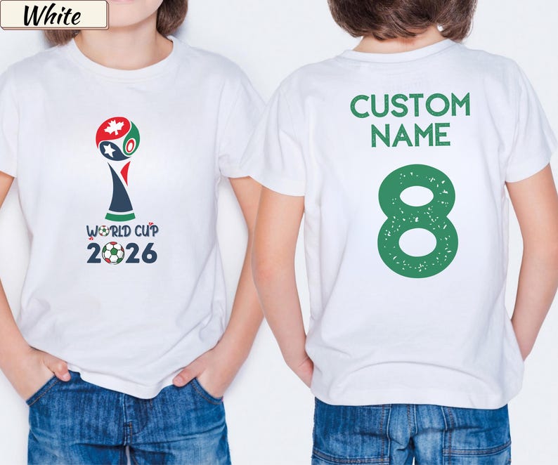 May include: A white short-sleeved t-shirt featuring a World Cup 2026 graphic on the front with a soccer ball and maple leaf icon. The back of the shirt displays the text CUSTOM NAME in green above a large green number 8 with a distressed texture.