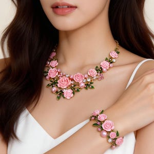 Può includere: Un set di gioielli floreali con collana e bracciale. La collana e il bracciale sono adornati con decorazioni a forma di rosa rosa, foglie verdi e perle finte. I gioielli hanno una base in metallo dorato.