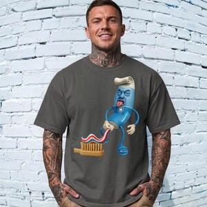 Op de afbeelding: Een antracietgrijs T-shirt met korte mouwen en een afbeelding van een blauwe antropomorfe tandpastatube die rood-wit-blauw gestreepte tandpasta op een beige tandenborstel knijpt. De tube heeft een gezicht, armen, benen en draagt blauwe sandalen.