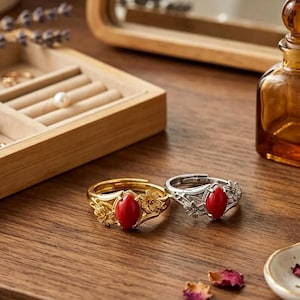 May include: Two adjustable rings featuring a marquise-cut red stone center and floral detailing on the band. One ring is finished in a gold tone, while the other is finished in a silver tone. Both rings have an open back design for size adjustment.