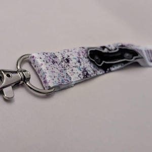 May include: A keychain with a silver clasp and a white strap. The strap has a black car graphic and a purple splatter design. The text "WERE DRIVIN" is printed on the end of the strap.