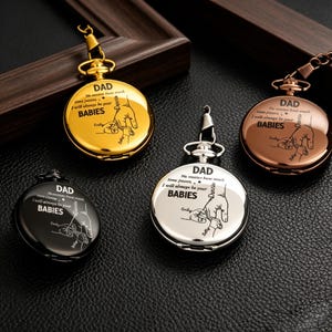Pode incluir: Quatro relógios de bolso em ouro, preto, prata e bronze. Cada relógio tem a palavra "DAD" no topo, com o texto "No matter how much time passes, I will always be your BABIES" e um desenho de uma mão segurando a de um bebê.