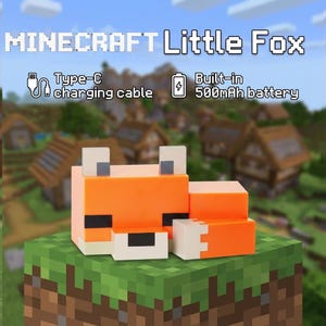 Op de afbeelding: Een oranje, witte en zwarte Minecraft Little Fox figuur, met een Type-C oplaadkabel en een ingebouwde 500mAh batterij. De figuur staat op een gepixeld groen en bruin oppervlak, met het Minecraft logo bovenaan.