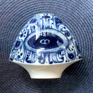 May include: A white ceramic vase with a blue and white abstract design. The vase is shaped like a mushroom and has a wide, flat top.