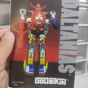 May include: A colorful image of a GoDaiKin Dalas toy robot. The robot has a lion's head and is primarily red, yellow, blue, and white. The image also includes the text "DALAS" and "GoDaiKin".