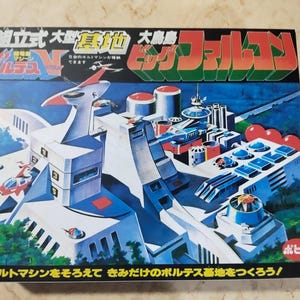 Puede incluir: Una caja de modelo vintage de Voltes V Big Falcon. La caja presenta una colorida ilustración de una base futurista con una gran estructura blanca, detalles en rojo y el texto japonés "Voltes V" y "Big Falcon".