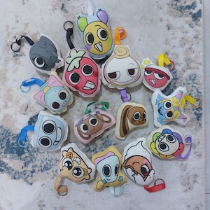 Puede incluir: Una colección de llaveros de peluche con varios diseños de personajes de dibujos animados. Los llaveros presentan una variedad de colores, incluyendo rosa, azul, amarillo y blanco. Cada llavero tiene un lazo para sujetar y está hecho de tela suave.