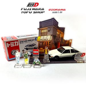 May include: A diorama set featuring a white Initial D AE86 Trueno model car, scale 1:64, with a Fujiwara Tofu Shop backdrop. Includes miniature figures and a Tomica box. The set has Japanese text.