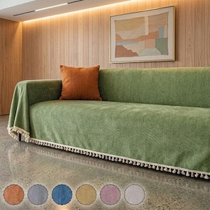 May include: A sage green sofa cover with a textured weave and a cream-coloured fringe trim along the bottom edge. A solid burnt orange square throw pillow rests on the sofa. Six small circular colour swatches are displayed at the bottom.