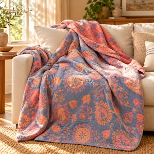 May include: A soft, quilted throw blanket featuring a repeating floral and medallion pattern in shades of muted blue and vibrant coral orange. The fabric has a textured, stitched appearance with a consistent design across the entire surface.