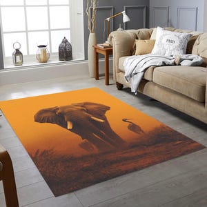 May include: An orange area rug featuring an elephant and a bird silhouette against a sunset backdrop. The rug has a rectangular shape and is placed in a living room setting, near a sofa and window.