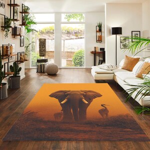 May include: A rectangular area rug featuring an elephant and a bird in a savanna landscape. The rug has a warm orange and brown color palette, with the elephant as the central focus. The rug is placed on a hardwood floor.