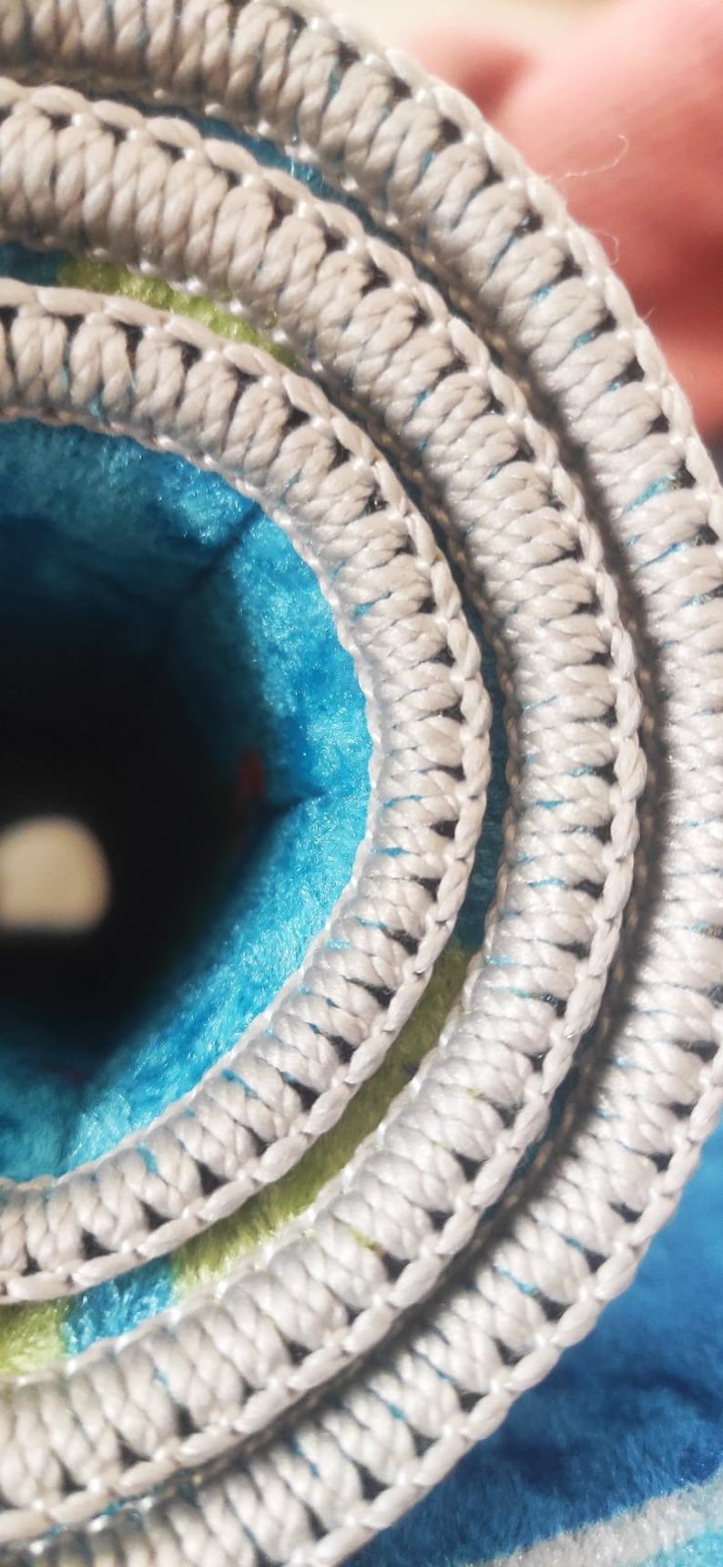 May include: Close-up of a rolled-up rug with a white, textured border. The rug's interior features a vibrant blue and green pattern. The border is made of a thick, woven material.