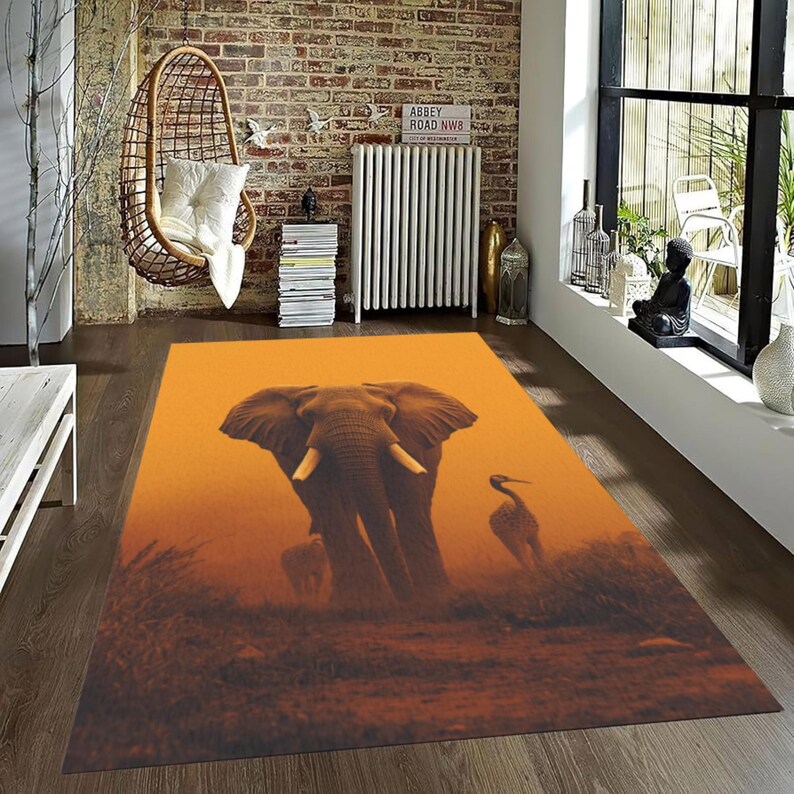 May include: Rectangular area rug featuring an elephant and a bird in a warm, orange-toned landscape. The rug's design includes a large elephant with visible tusks and a bird silhouette, creating a nature-inspired theme for home decor.