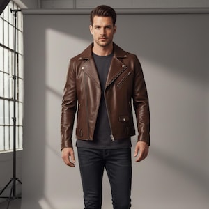以下が含まれることがあります： クラシックなバイカースタイルの茶色のレザージャケット。ノッチドラペルカラー、非対称ジッパー開閉、複数のポケットが特徴です。モデルはグレーのTシャツと濃い色のジーンズを着用しています。
