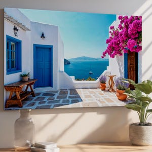 Può includere: Stampa su tela di una scena costiera con edifici bianchi, porte e finestre blu. Sono visibili una panchina in legno e piante in vaso. Il mare e il cielo blu creano un'atmosfera serena, con una barca a vela in lontananza.