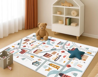 Puede incluir: Alfombra de juego blanca con un diseño de ciudad colorido con carreteras, edificios y vehículos. Un oso de peluche marrón y un cojín azul en forma de estrella están sobre la alfombra. La alfombra está sobre un suelo de madera clara.