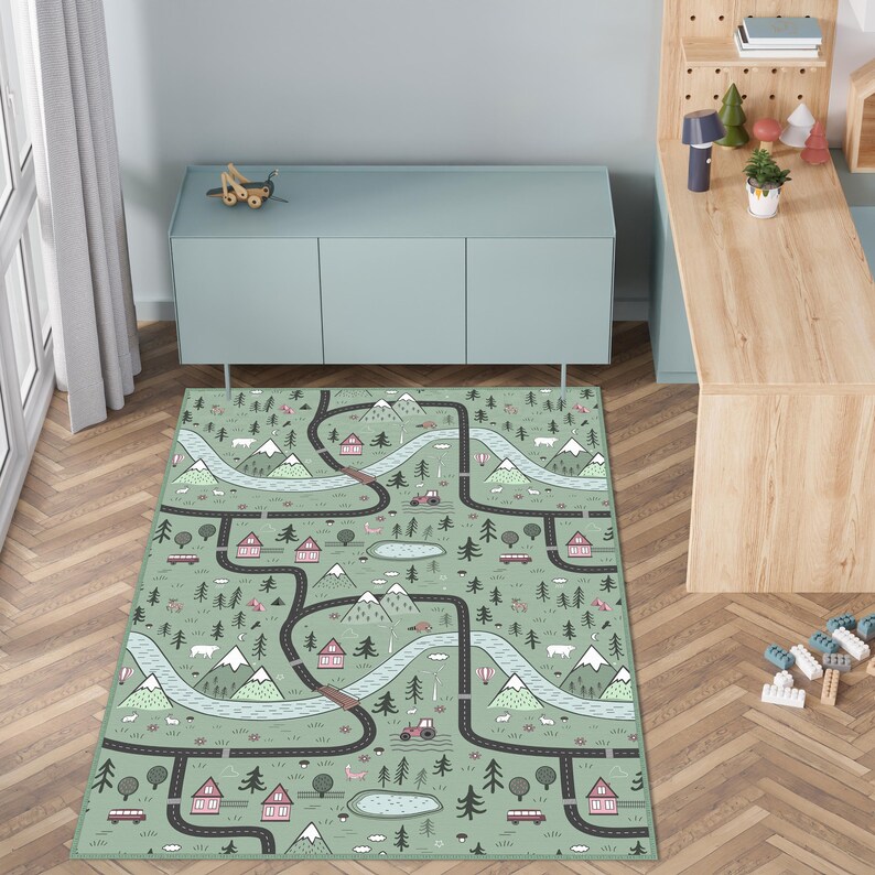 May include: A rectangular play rug with a road map design. The rug features a light green background with roads, rivers, mountains, houses, and trees. The design includes cars, a tractor, and other vehicles. The rug is placed on a wooden floor.