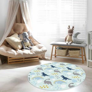 May include: A round, light blue rug with a repeating pattern of cartoon dinosaurs in gray and navy blue, with white clouds and yellow accents. The rug is in a child's room, with a canopy chair and a bench with stuffed animals.