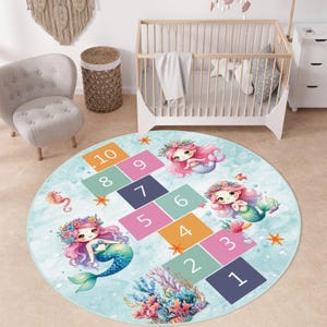 May include: A round, light blue hopscotch rug featuring a mermaid theme. The rug has a hopscotch grid with numbers 1-10, and illustrations of mermaids, coral, and starfish. The rug is designed for children's play.