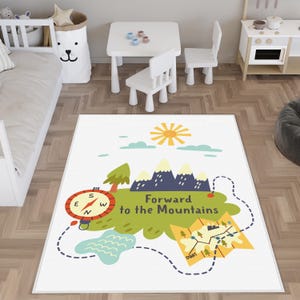 Könnte beinhalten: Weißer rechteckiger Teppich mit einem farbenfrohen, illustrierten Kartendesign. Der Teppich zeigt einen Kompass, Berge, eine Sonne und den Text "Forward to the Mountains". Das Design beinhaltet eine Karte und einen gepunkteten Pfad.