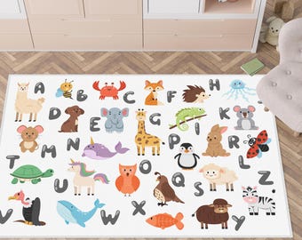 May include: A white rectangular rug featuring the alphabet and colorful cartoon animals. Each letter of the alphabet is paired with an animal illustration, such as a llama for A, a bee for B, and a crab for C. The rug is placed on a wooden floor.