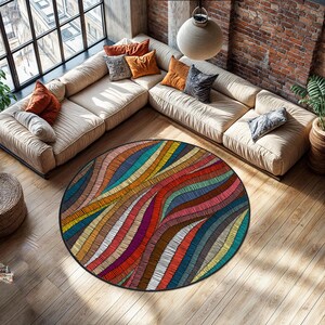 Op de afbeelding: Een rond vloerkleed met een levendig, abstract ontwerp. Het kleed heeft een zwarte rand en een patroon van kleurrijke, golvende lijnen in tinten rood, oranje, geel, groen, blauw en paars. Het ligt op een houten vloer.