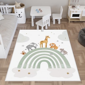 Può includere: Tappeto rettangolare per bambini con un design ad acquerello con un arcobaleno verde, nuvole e stelle. Il tappeto presenta animali dei cartoni animati tra cui una giraffa, un leone, un elefante, una scimmia e un ippopotamo. Il tappeto è bianco con dettagli verdi e oro.