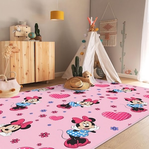 Puede incluir: Alfombra rectangular rosa con un patrón repetido de Minnie Mouse, corazones y flores. Minnie Mouse se muestra con su atuendo clásico con un vestido de lunares y un lazo grande. La alfombra está diseñada para una habitación infantil.