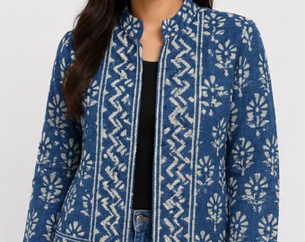 May include: A blue jacket with a white floral and chevron pattern, featuring a mandarin collar, long sleeves, and an open front design. The garment is layered over a black top and blue denim jeans, showcasing a structured fit and textured fabric.