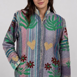 Könnte beinhalten: Bunte, gesteppte Jacke mit Reißverschluss. Die Jacke hat vertikale Streifen in Blau-, Rosa- und Lilatönen. Sie ist mit gestickten grünen Blättern, goldenen Herzen und roten Blumen verziert. Die Jacke hat lange Ärmel.