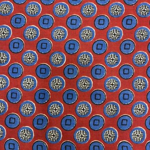 Könnte beinhalten: Nahaufnahme eines Stoffes mit einem sich wiederholenden Muster aus blauen Kreisen und Quadraten auf rotem Hintergrund. Jeder Kreis enthält ein weißes und schwarzes kreuzartiges Design. Der Stoff hat ein gleichmäßiges, symmetrisches Design.