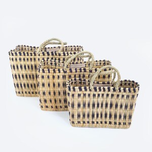 May include: Three woven rectangular baskets with handles. The baskets are made of natural-colored fibers with a repeating pattern of dark blue diamond shapes. The handles are made of twisted rope.