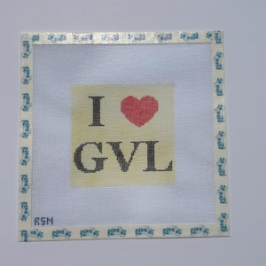 以下が含まれることがあります： 黒い文字と赤いハートで「I ♥ GVL」と書かれた正方形のニードルポイントキャンバス。キャンバスは、青で「RUNNING」という単語が印刷された白いボーダーで囲まれています。