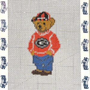 May include: Needlepoint of a teddy bear wearing a red sweater with a white and black "G" logo, blue jeans, and a red and black cap. The background is white with a grid pattern. The border has the text "RUNNING" repeated.