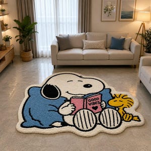 May include: A tufted area rug featuring a white cartoon dog with a black ear, wearing a blue blanket, reading a pink book with the text GOOD VIBES and a black heart icon, accompanied by a small yellow bird character on a white background.