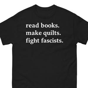 Puede incluir: Camiseta negra con texto blanco: "read books. make quilts. fight fascists." La camiseta tiene cuello redondo y mangas cortas. El texto está centrado en la parte delantera de la camiseta.