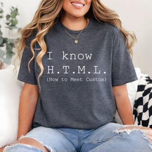 Pode incluir: Uma t-shirt de manga curta em cinzento mesclado escuro com o texto branco I know H.T.M.L. (How to Meet Custom) numa fonte sem serifa clara. A pe&ccedil;a tem um decote redondo cl&aacute;ssico e um corte padr&atilde;o feito de tecido macio e texturado.